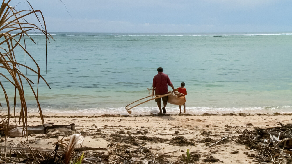 Ein Mann und ein Junge tragen ein Holzboot zum Meeresufer.