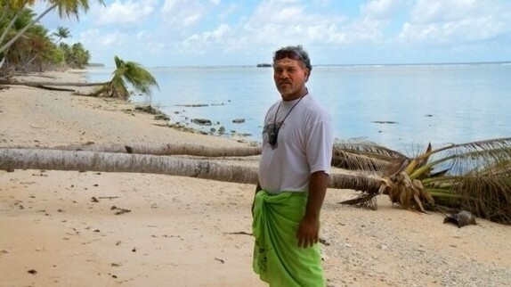 Ein Bewohner von Tuvalu steht am Meeresufer und hinter ihm ist eine gefallene Palme zu sehen.
